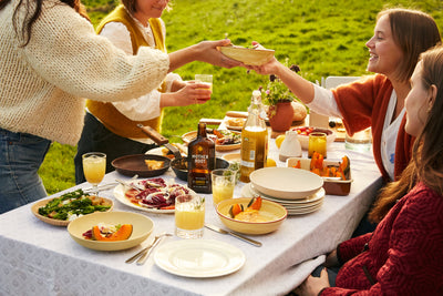 Four women enjoying salads and juice together at an outdoor table on a sunny day.