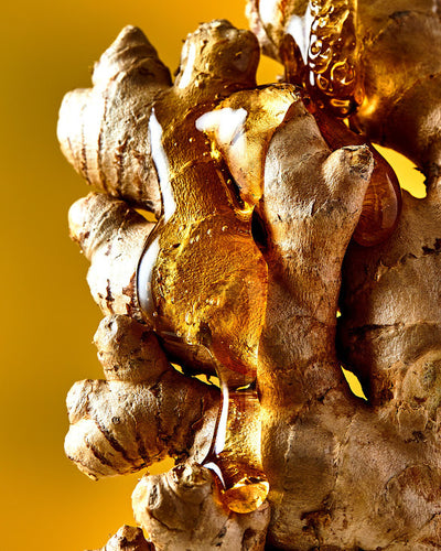 Close-up of honey pouring over fresh ginger root against a vibrant yellow background.