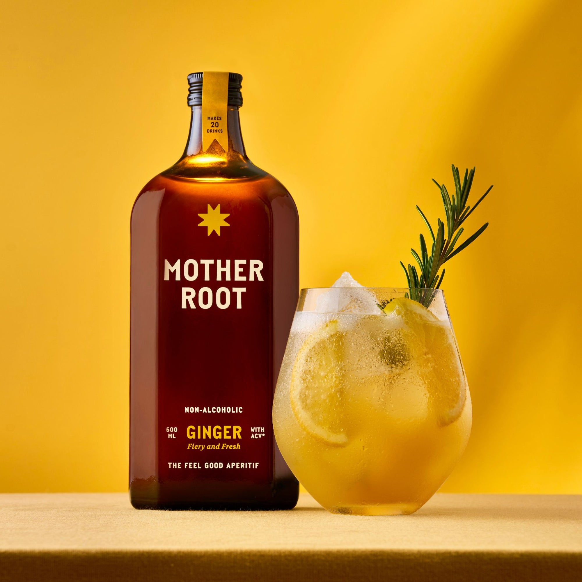 A bottle of Mother Root Ginger from Mother Root sits next to a glass of iced ginger drink with apple cider vinegar and rosemary, all set against a bright yellow background.