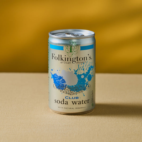 A can of Mother Root Soda Water [8 x 150ml], with a blue and gold design, rests on a tan surface against a mustard yellow background. The label displays splashing water and promotes light, fresh bubbles with natural minerals.
