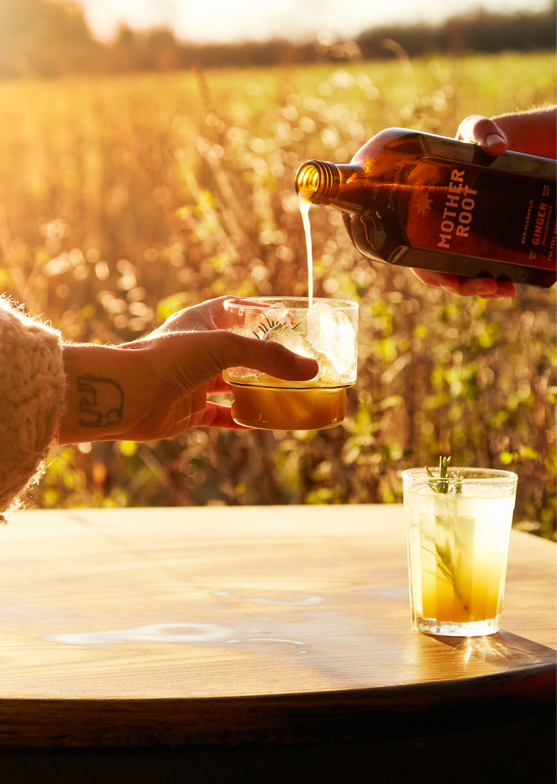 A refreshing drink is poured over ice outdoors, sunlight glimmering and fields stretching into the distance.