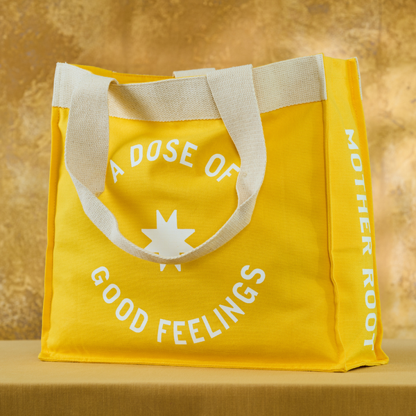 Mother Root yellow tote bag with side pockets, white text on warm brown background: "A DOSE OF GOOD FEELINGS.